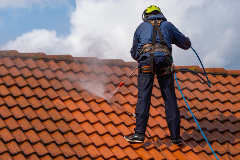 A Person Wearing Safety Gear And Cleaning A Roof